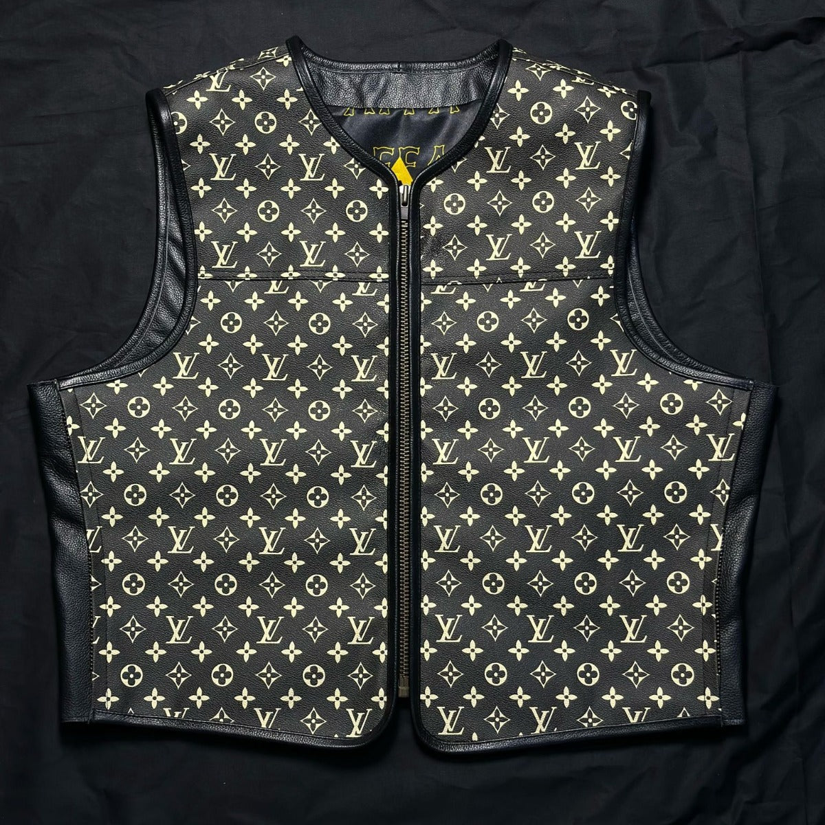 A Louis Vuitton monogram quilted vest with black leather trim, laid flat on a black fabric background.