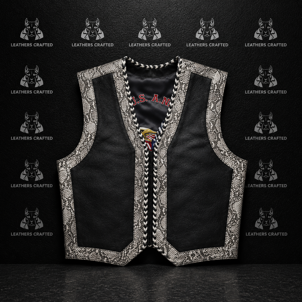A black leather vest with ornate silver and white embroidered borders, displayed against a dark textured background with repeating 'Leathers Crafted'  logos.